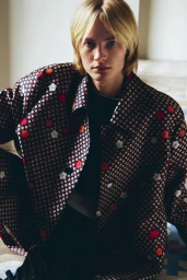 Model Leander Straub wearing a dark floral pattern jacket looking directly into the camera in an indoor setting.