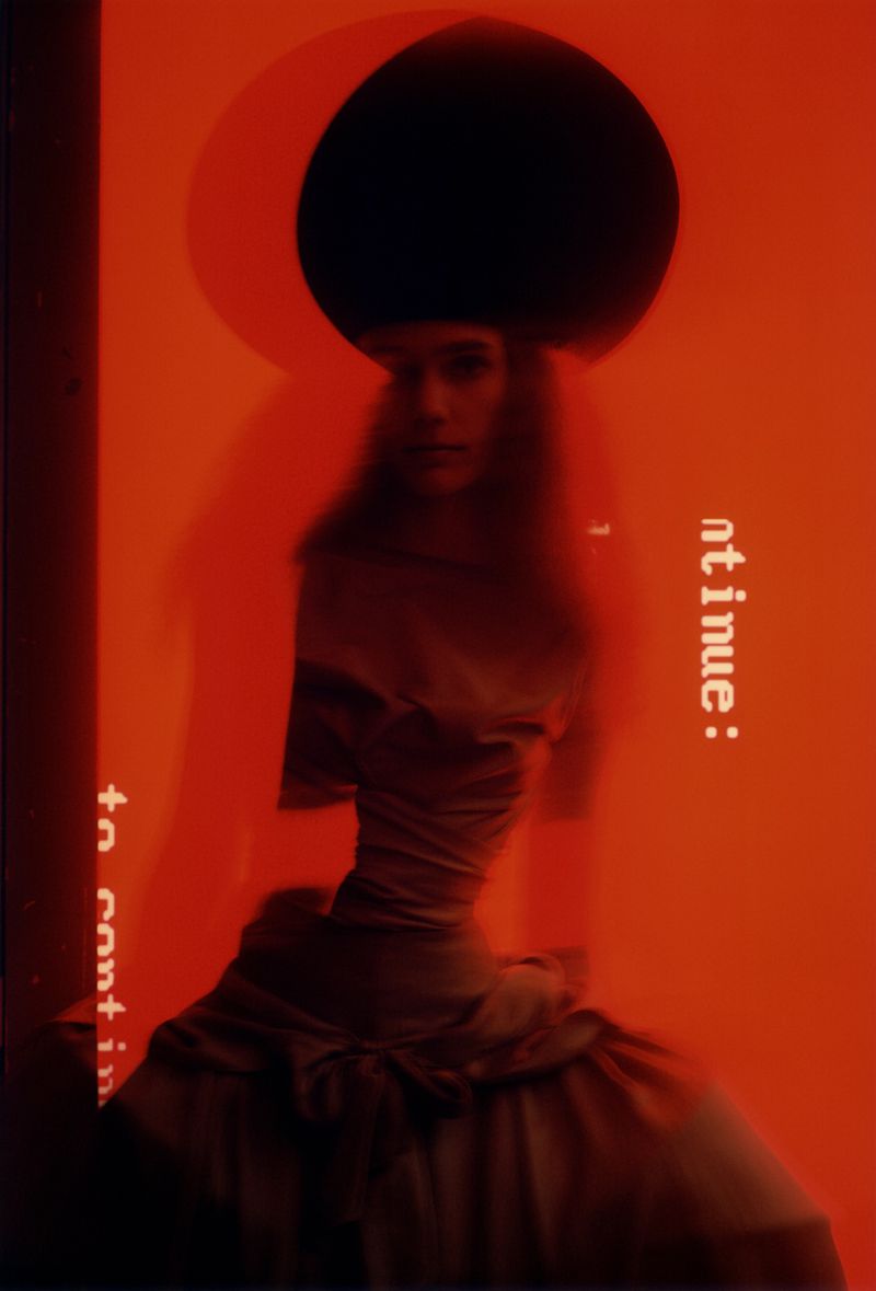 A woman in a dress poses in a studio with a black circle in the background, illuminated by orange lighting and with text overlay.