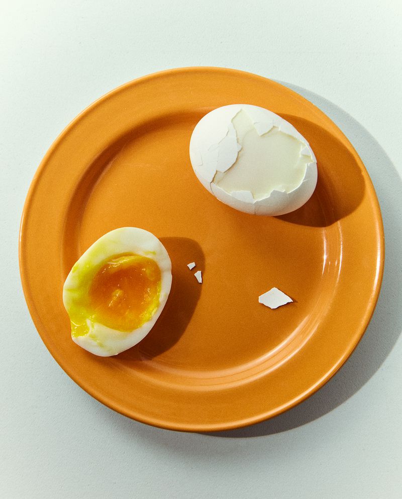 Overhead shot of halved, peeled boiled egg on an orange plate against a white backdrop, showing the vibrant yolk and egg white.
