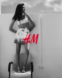Mariana Goncalves standing on a chair against a wall wearing a printed crop top and mini skirt in an H&M campaign.