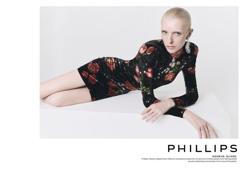 Elegant woman in a floral print dress lying on a white platform, wearing ornate earrings, in a studio with soft lighting.