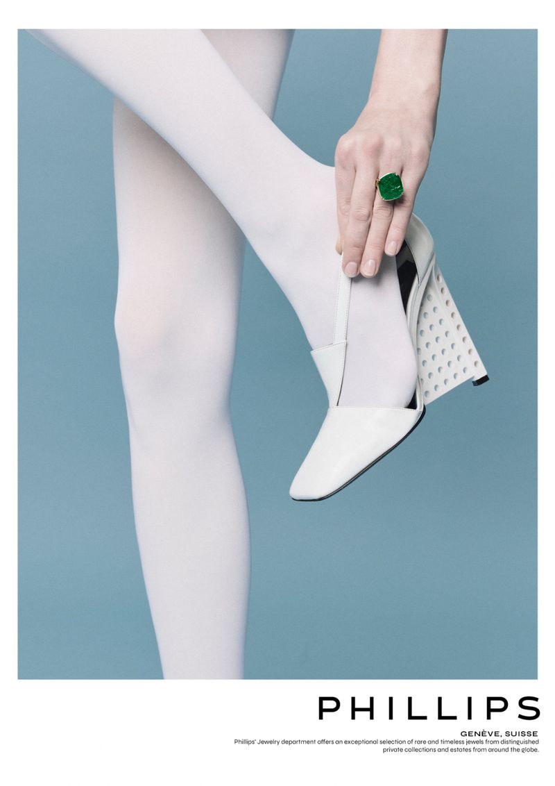 Fashion editorial shot featuring a female model wearing white tights and holding a white high heel, showcasing a large green ring.