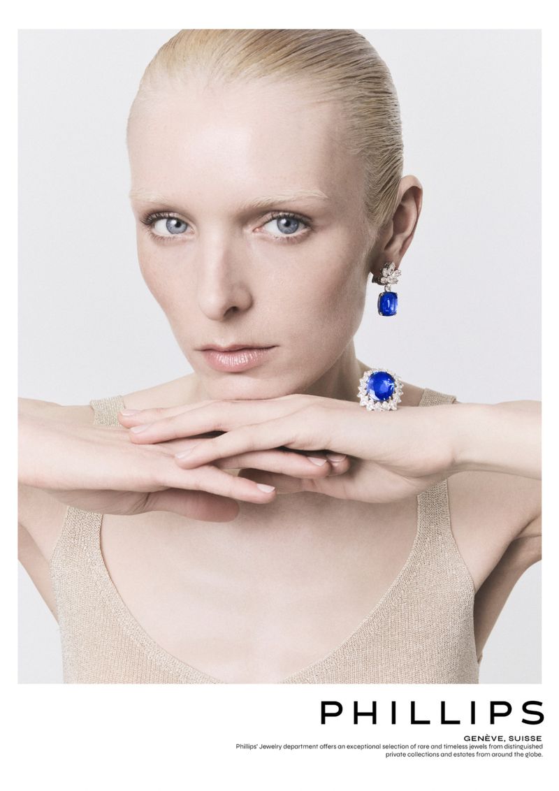 Close-up of an adult female model with blonde hair wearing sapphire and diamond jewelry against a plain white background in a studio.