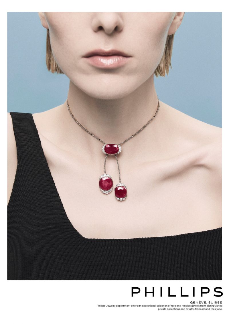 Woman wearing ruby and diamond necklace. The elegant jewelry stands out against the light blue background and her simple black dress.