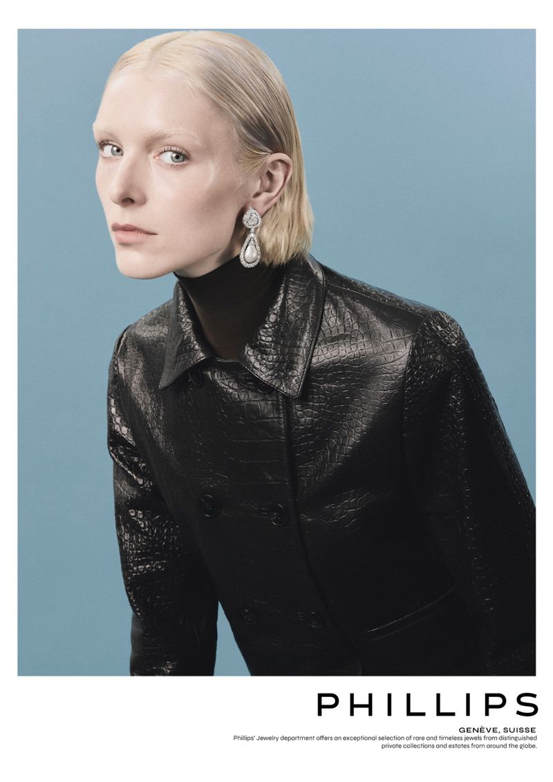 Fashion portrait of a fair-skinned woman with blonde hair wearing statement earrings and a glossy black leather jacket against blue.