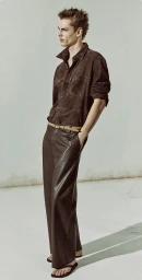 Model Esteban Monbaliu wearing a brown suede shirt and wide-leg leather trousers against a pale wall for Zara.