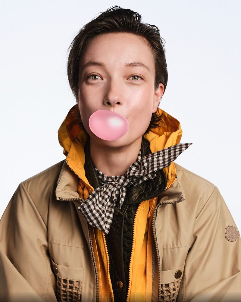Close-up of a person with bubblegum. A young adult with short, dark hair, wearing a jacket, blowing bubblegum, set against a white backdrop.