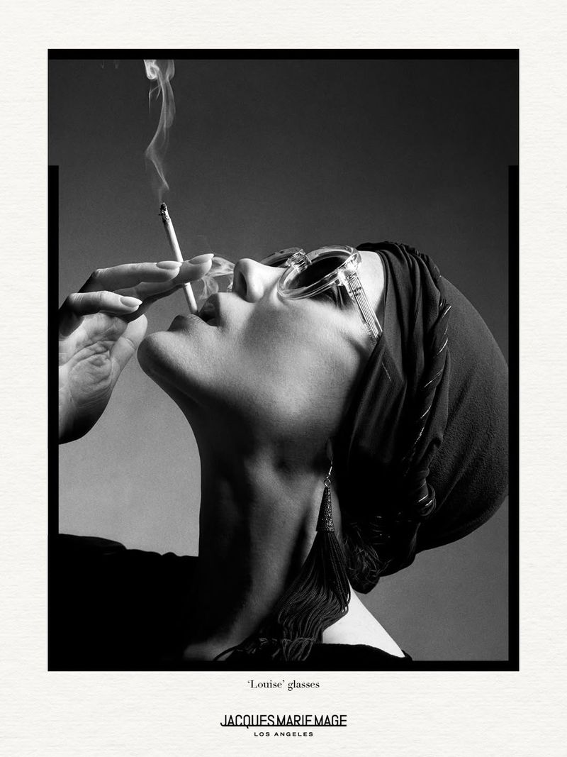 Monochrome portrait of a woman with sunglasses smoking, with elegant jewelry, against a neutral backdrop and Jacques Marie Mage logo.