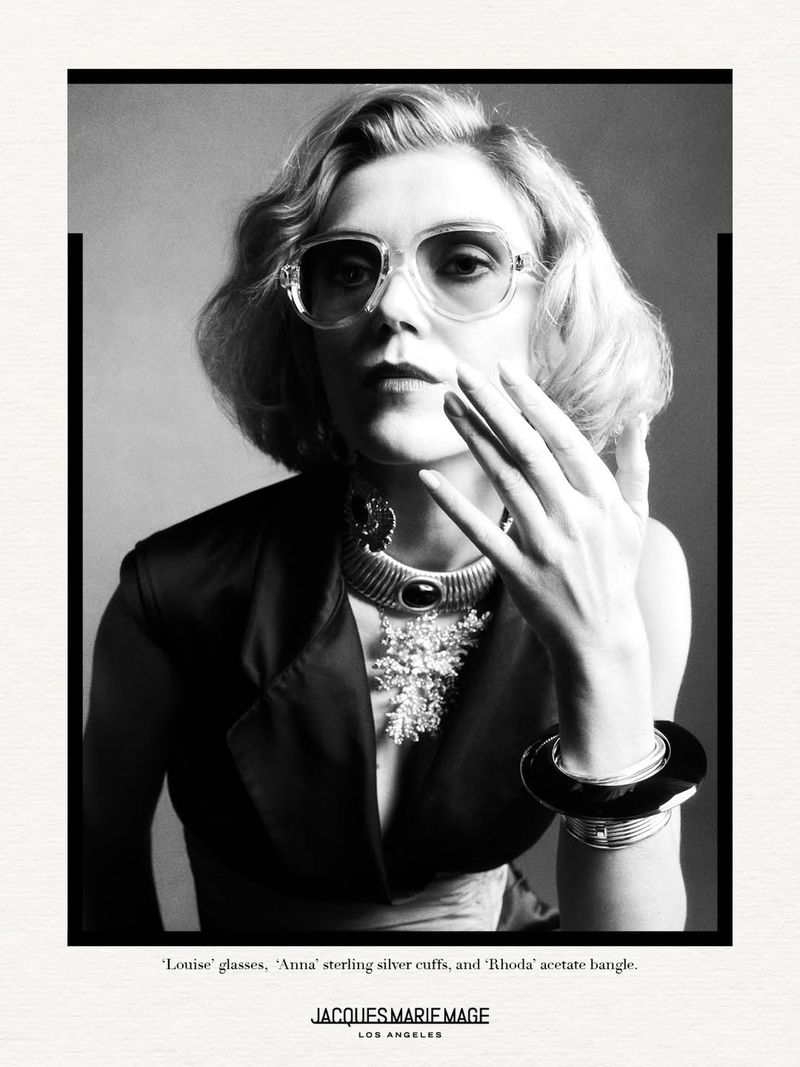 Black and white portrait of a woman wearing glasses and jewelry. She is wearing a jacket. The style is editorial and fashion forward.