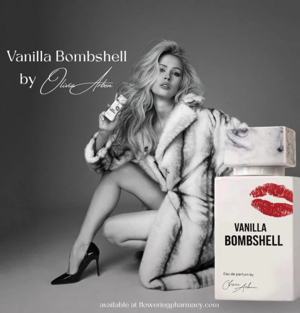 A blonde woman in a fur coat holds a perfume bottle, seated next to a larger fragrance bottle in a studio shot for beauty product advertising.