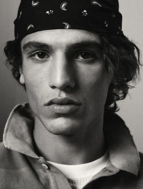 Close-up black and white portrait of a young adult male with a bandana, collared shirt, and light skin. Focus on his face.