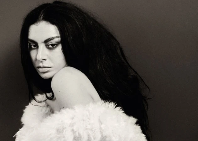 Monochromatic portrait of a woman with dark hair and makeup, draped in a white, furry garment against a dark grey backdrop.