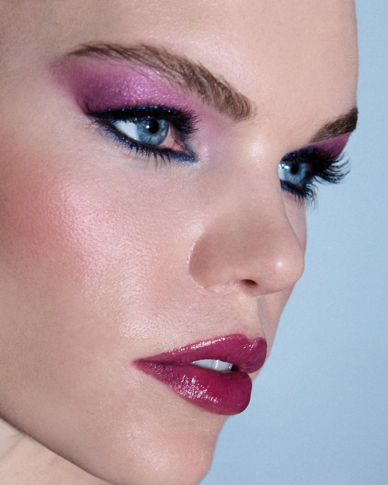 Close-up of woman's face with pink eyeshadow, eyeliner, and dark lipstick against a blue background showcasing beauty and makeup.