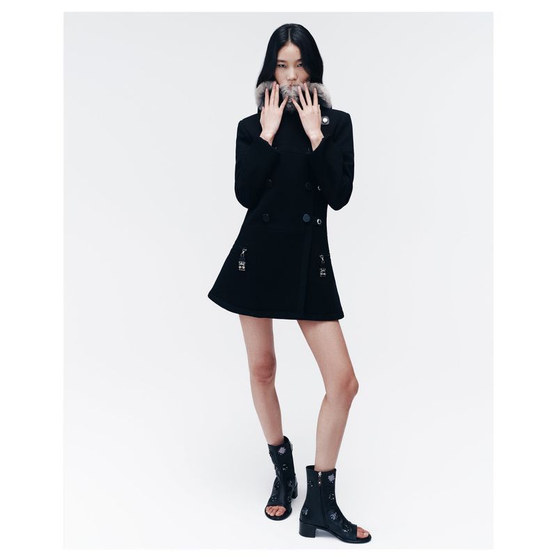 Elegant Asian model showcasing a black wool coat with fur collar and peep-toe ankle boots in a minimalist white studio setting.