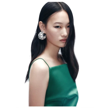 Asian woman portrait in a green dress with black hair and statement earrings against a white backdrop in a fashion studio shot.
