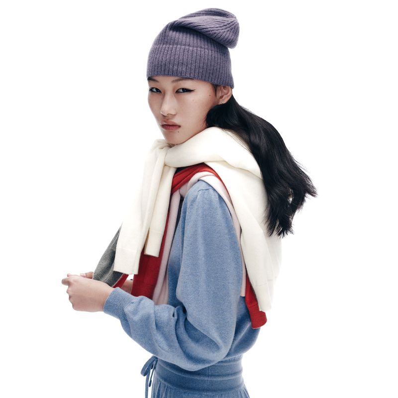 A portrait of an Asian woman wearing a blue top, hat, and scarf. Studio shot with white background. Soft lighting.