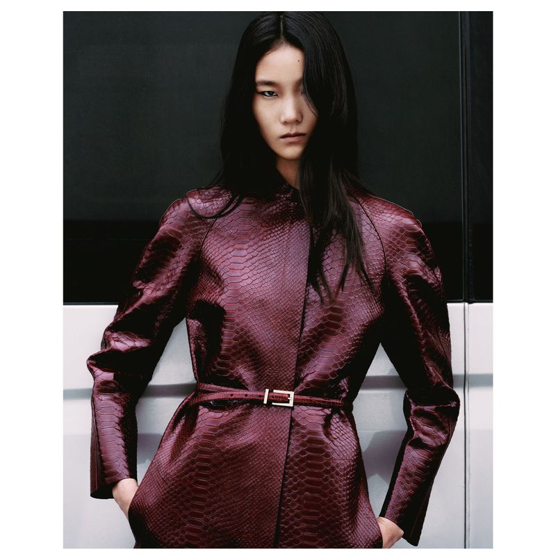 Elegant Asian woman in reptile-patterned maroon jacket, with hands in pockets and a sleek modern backdrop, Fashion editorial shot.