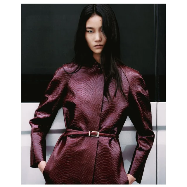 Elegant Asian woman in reptile-patterned maroon jacket, with hands in pockets and a sleek modern backdrop, Fashion editorial shot.