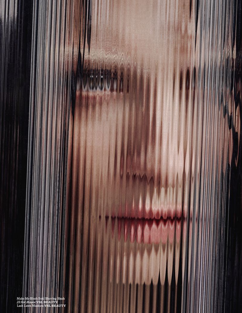 Close-up portrait of a woman's face partially obscured by vertical, textured glass, creating a distorted and artistic effect.