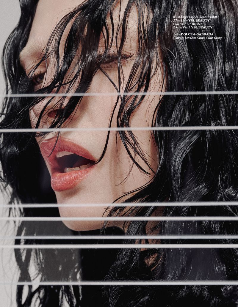 Close-up beauty shot of a woman with wet, dark hair, partially obscured by Venetian blinds, showing an open mouth with coral lipstick.