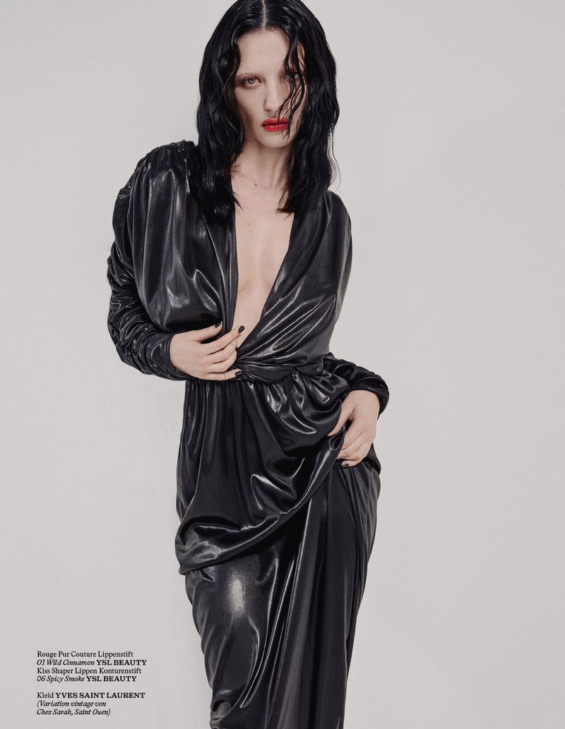 Elegant woman in black dress with deep V-neck posing in a studio. Red lipstick and dark hair add to the high fashion aesthetic.