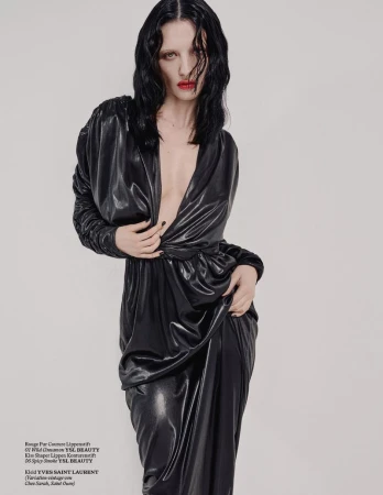 Elegant woman in black dress with deep V-neck posing in a studio. Red lipstick and dark hair add to the high fashion aesthetic.