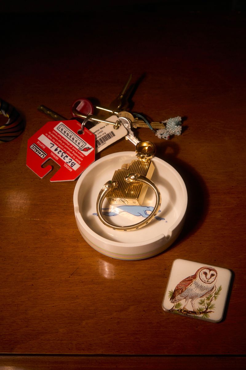 A key ring with multiple keys sits in a round dish on a wooden surface next to a square tile with an owl design.