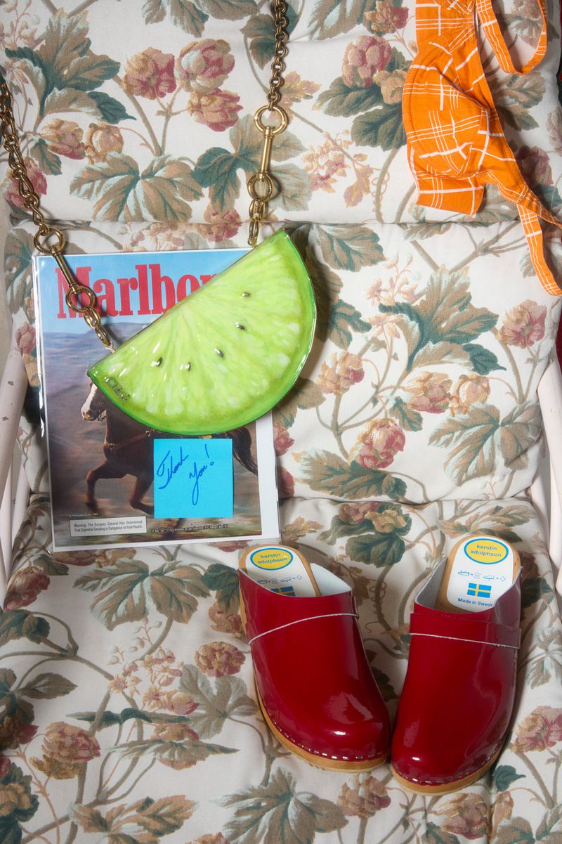 Still life arrangement featuring red clogs, magazine, lime purse, and patterned fabric backdrop creating a visually striking composition.