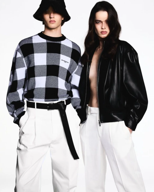 Two fashion models in black and white outfits pose in front of a bright white backdrop, showcasing modern, stylish attire.
