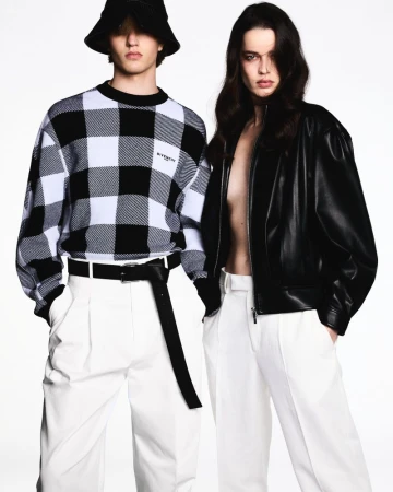 Two fashion models in black and white outfits pose in front of a bright white backdrop, showcasing modern, stylish attire.