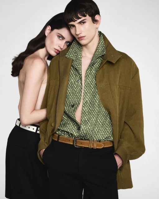 A stylish fashion portrait features a male and female model posing in a studio setting, wearing olive green and black clothing.