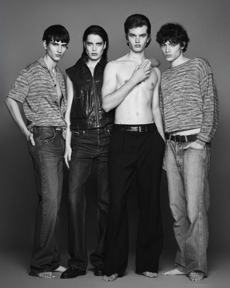 Four fashion models in a studio portrait showcasing clothing. Three male models wearing jeans and one female model wearing a leather vest.