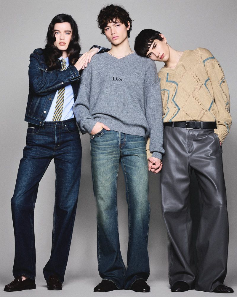 Three fashion models in a studio setting. One in a denim jacket, one in a grey sweater, and one in a patterned sweater. 