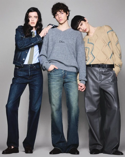Three fashion models in a studio setting. One in a denim jacket, one in a grey sweater, and one in a patterned sweater. 