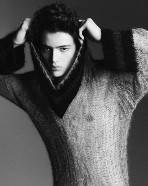 Portrait of a young adult man wearing a dark and light knit sweater, looking directly at the camera in a studio setting.