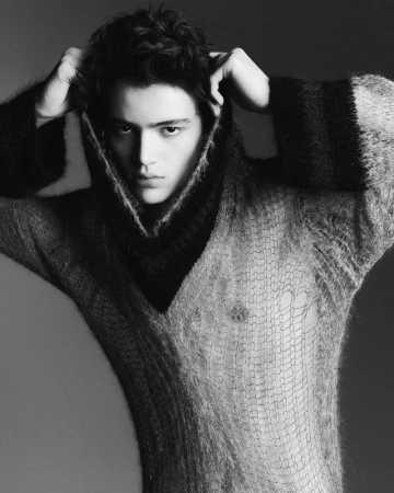 Portrait of a young adult man wearing a dark and light knit sweater, looking directly at the camera in a studio setting.
