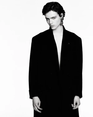 Monochrome portrait of a young male model wearing a dark oversized blazer against a plain white background.