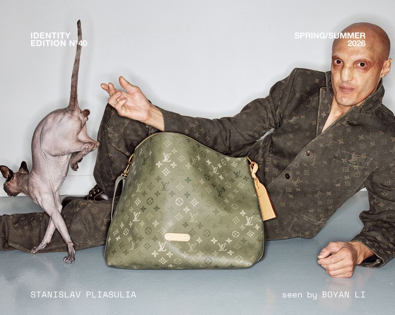 Fashion editorial featuring a bald man in a monogrammed suit next to a hairless cat and a patterned handbag in a studio setting.