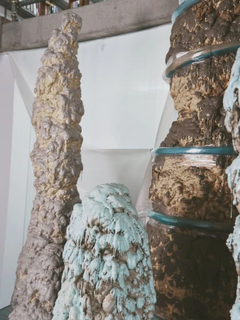 Unique rock sculptures with layered textures and shades of brown, beige, and blue stand against a simple white backdrop in a studio setting.