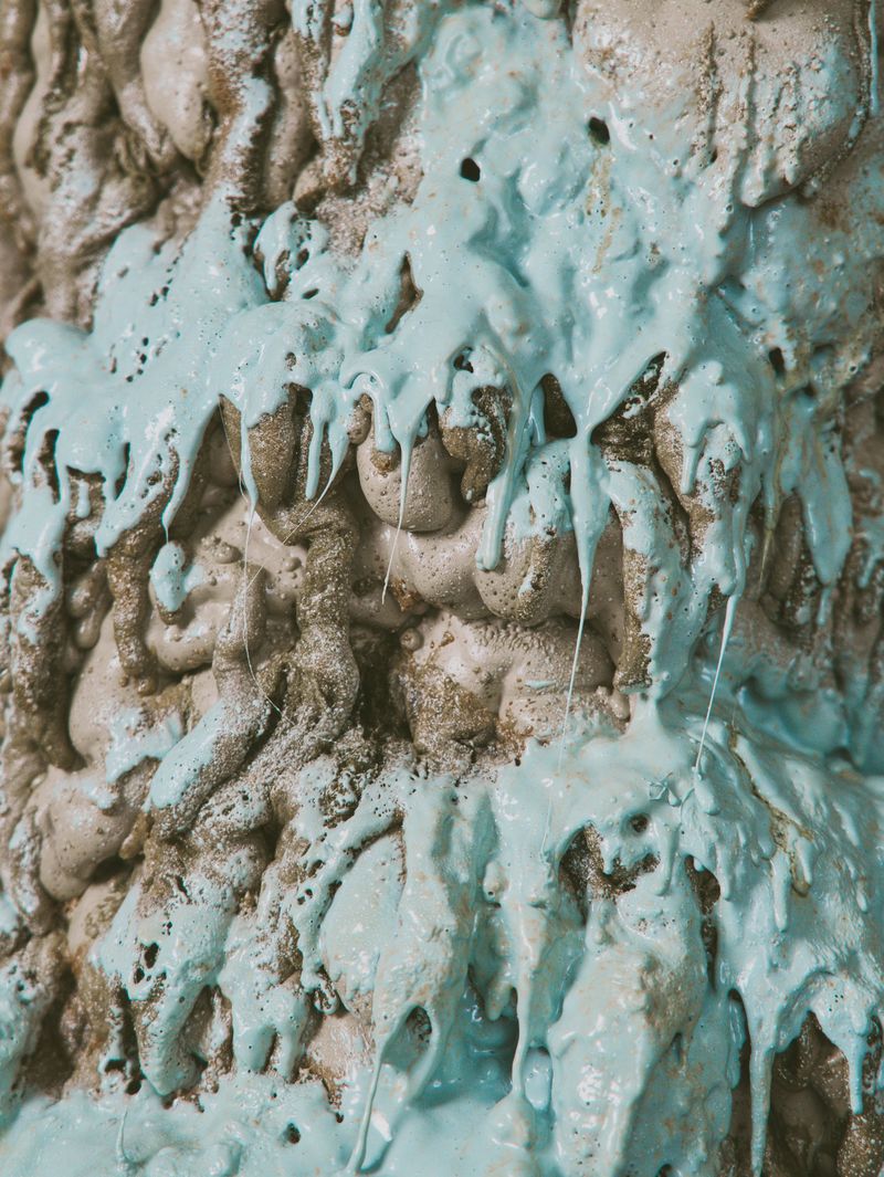 Abstract art features textured gray surface with drizzles of light-blue paint, showcasing an interplay of textures and subtle coloration.