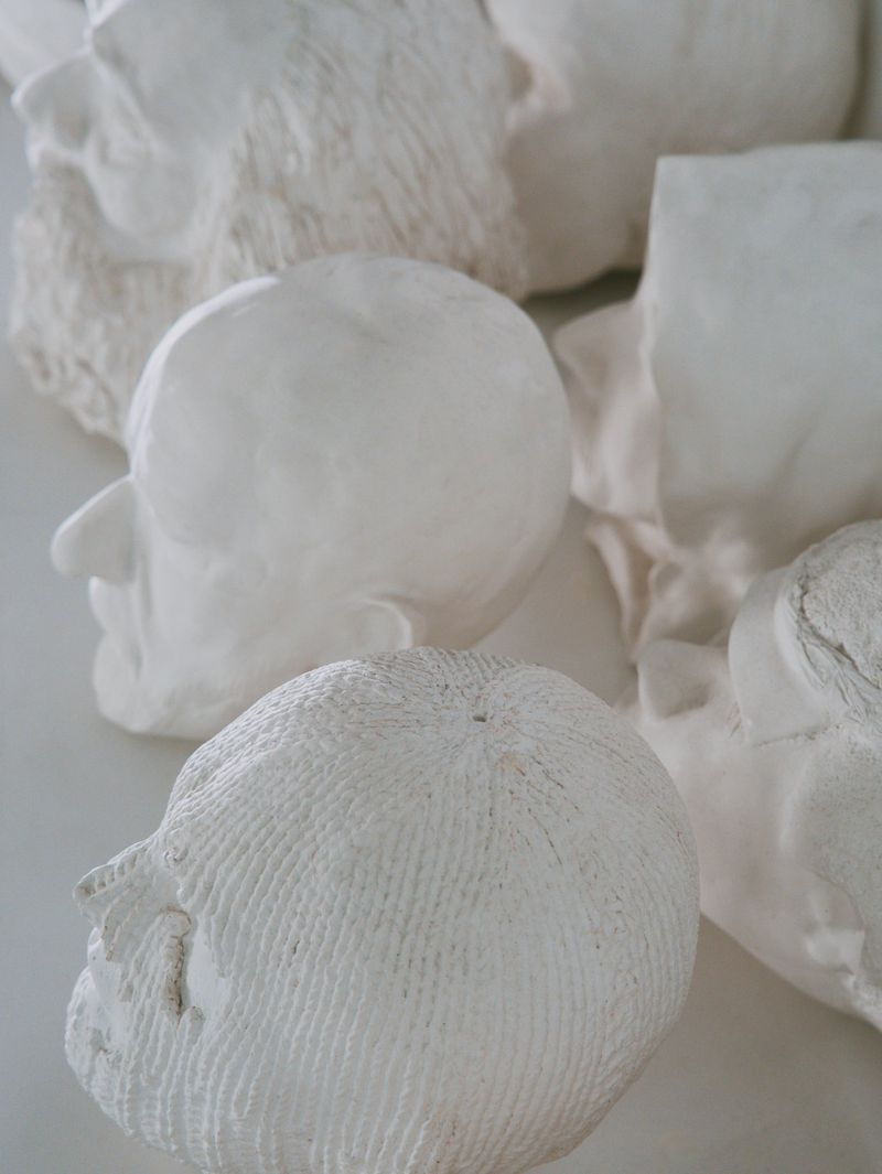 Collection of white plaster head sculptures with various textures and smooth surfaces, arranged indoors with a shallow depth of field.