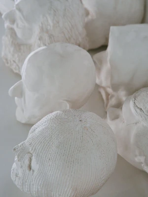Close-up overhead view of multiple white plaster head sculptures and carved bust fragments on a light surface.
