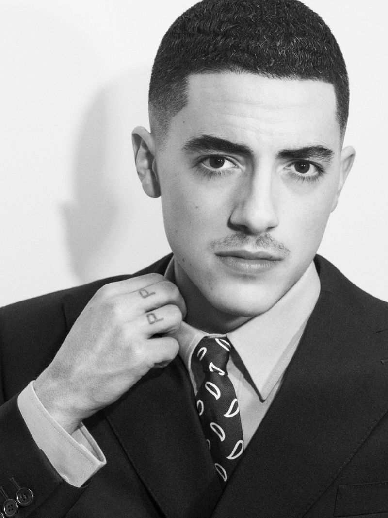Black and white portrait of a young adult man in a suit and tie, gazing directly at the camera, showcasing his haircut, and formal attire.