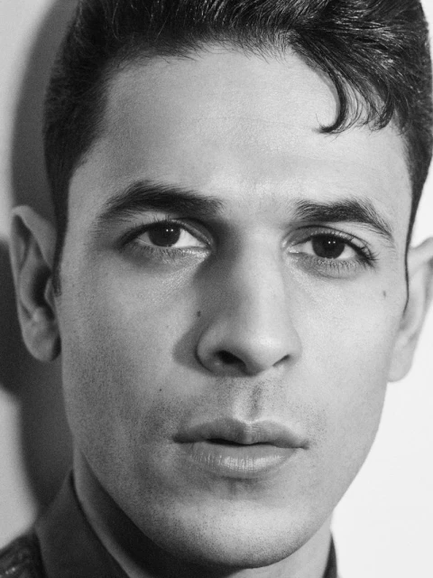 Black and white portrait of a man with short dark hair looking directly at the camera in front of a neutral background.