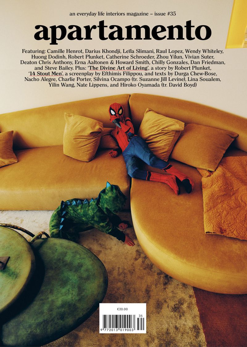 Magazine cover featuring child in Spiderman costume lounging on yellow couch with a plush dinosaur toy, copy of Apartamento magazine. 