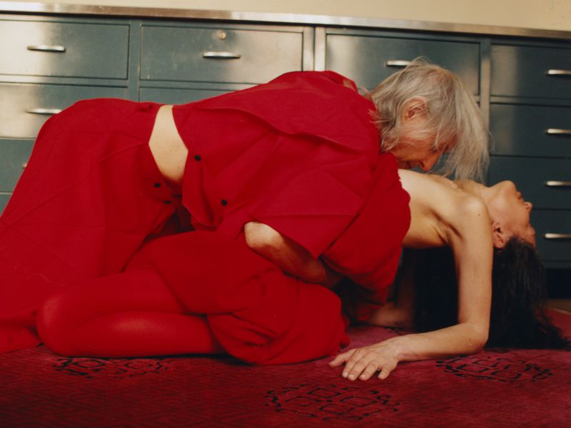 Striking photograph featuring an elderly person in a red outfit interacting with a younger individual in an indoor setting.