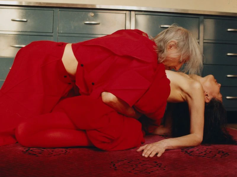 Striking photograph featuring an elderly person in a red outfit interacting with a younger individual in an indoor setting.