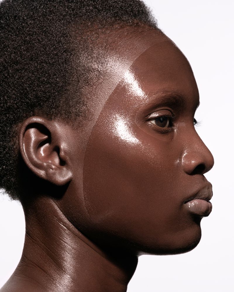 Close-up portrait of a dark-skinned woman showcasing radiant, glowing skin with a sleek hairstyle against a clean, white background.