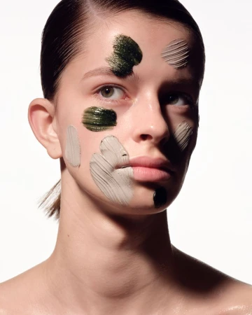 Close-up of a young woman's face with patches of different colored facial mask, set against a bright white background.