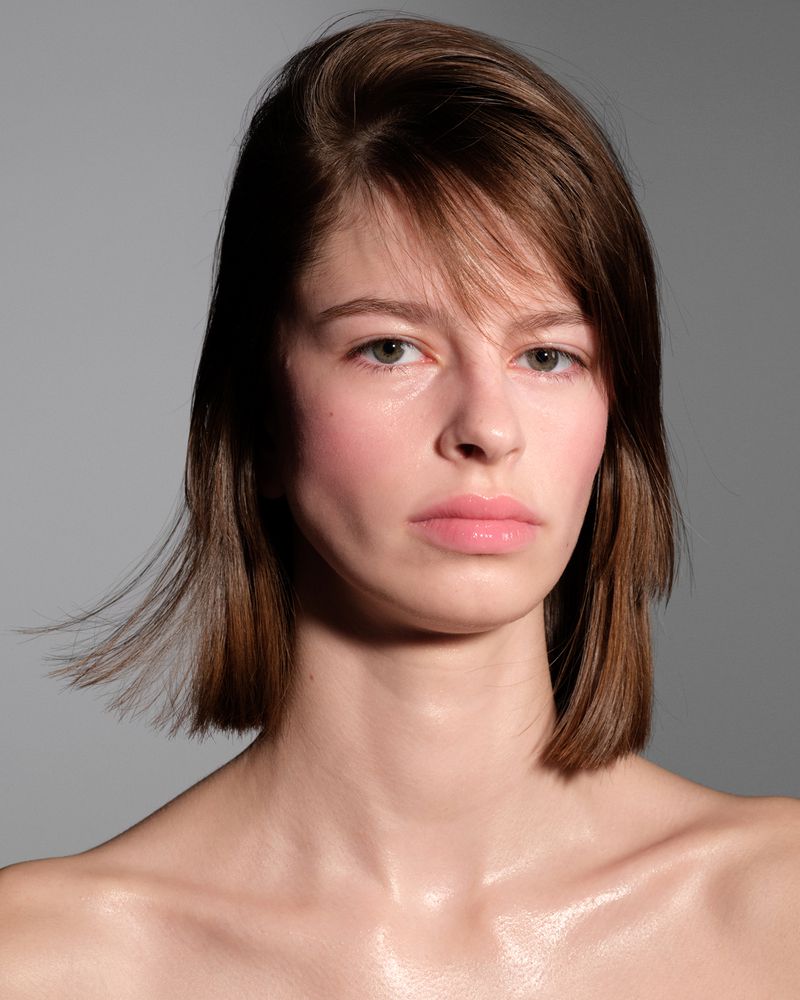 Close up portrait of a woman with short brown hair and natural makeup against a plain grey studio backdrop
